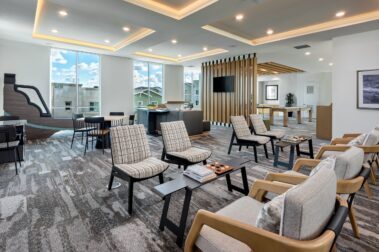 modern lobby image with dining tables and lounge tables flush with chairs and further back a couch with a tv viewing area and shuffleboard
