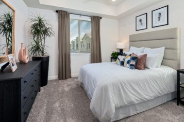 apartment bedrrom with curtains a queen bed with soft linens a cabinet and carpeting