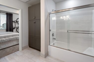 apartmnet bathroom with a bathroom shower with glass curtains closet and muted grey tones