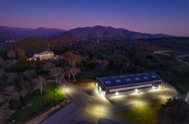 exterior evening shot of custom car warehouse developed by barken near a well lit mansion in the distance near hills