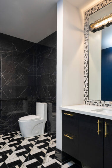 Luxury commercial restroom featuring a bold black marble tile wall, modern fixtures, and geometric floor tiling, part of the DV Kap Headquarters project by Barken.