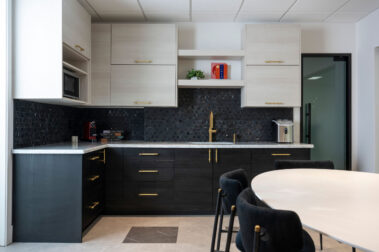 Contemporary office kitchenette with dark lower cabinets, light upper shelving, and a marble countertop, reflecting Barken's premium commercial build-out quality.