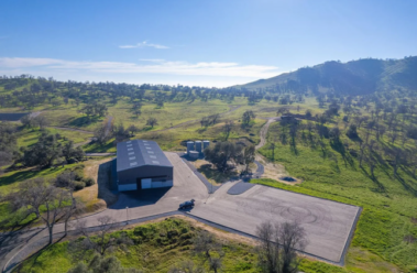 daytime exterior of custom car warehouse developed by barken construction in a secluded hills environment with lush greenery on a sunny day